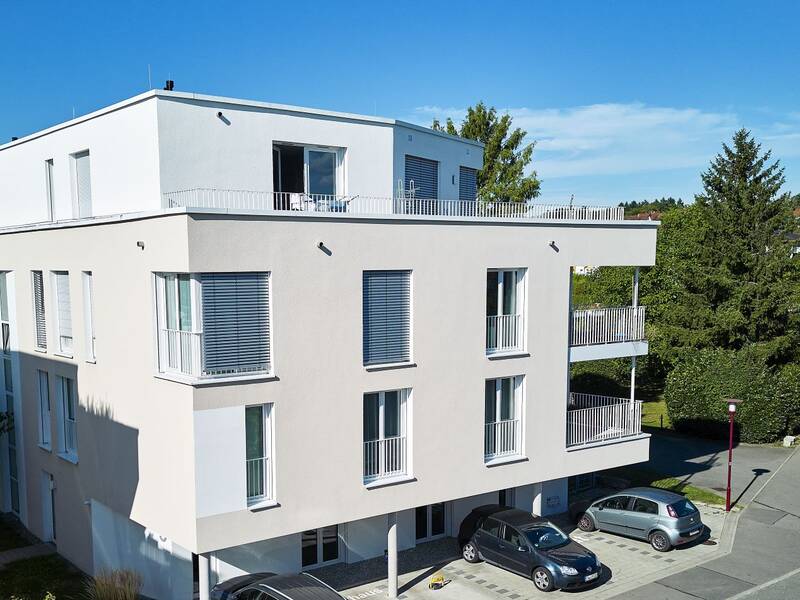 Ein modernes Gebäude mit Bäumen umgeben vor dem Gebäude befinden sich Parkplätze mit Autois
