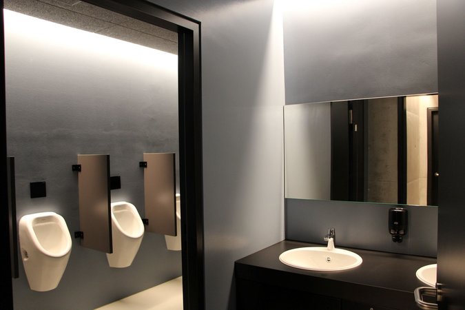 Ein modernes Badezimmer mit Waschbecken, großem Spiegel und nebeneinander angeordneten Urinalen.