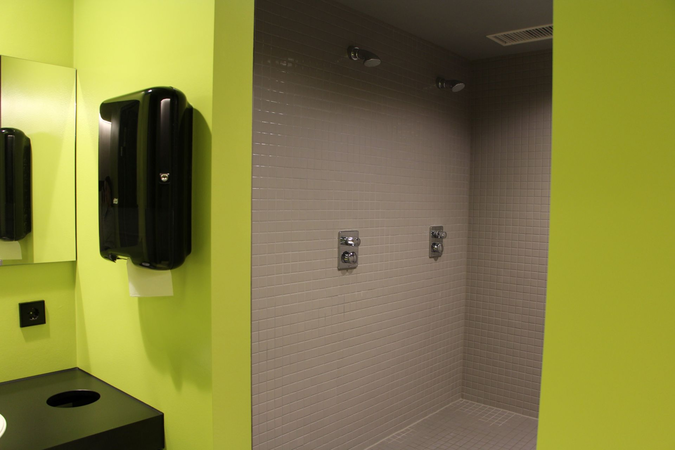 Ein Badezimmer mit grünen Wänden zeigt eine moderne Dusche mit grauen Kacheln und zwei Duschköpfen.