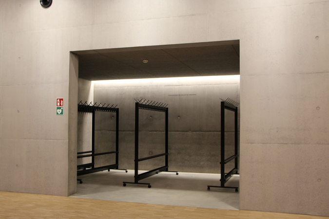 Ein leerer Garderobenbereich in einem modernen, minimalistisch gestalteten Raum mit grauen Wänden und freistehenden Kleiderständern.