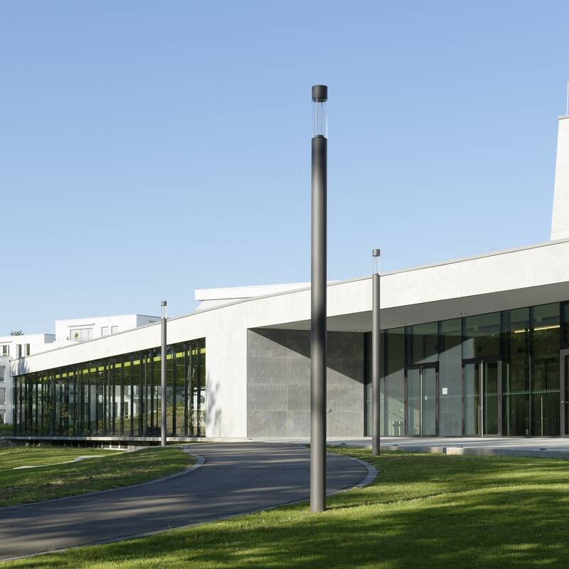 Ein modernes Gebäude mit Glasfronten und einem geschwungenen Weg im Vordergrund, umgeben von grünen Rasenflächen und Bäumen.
